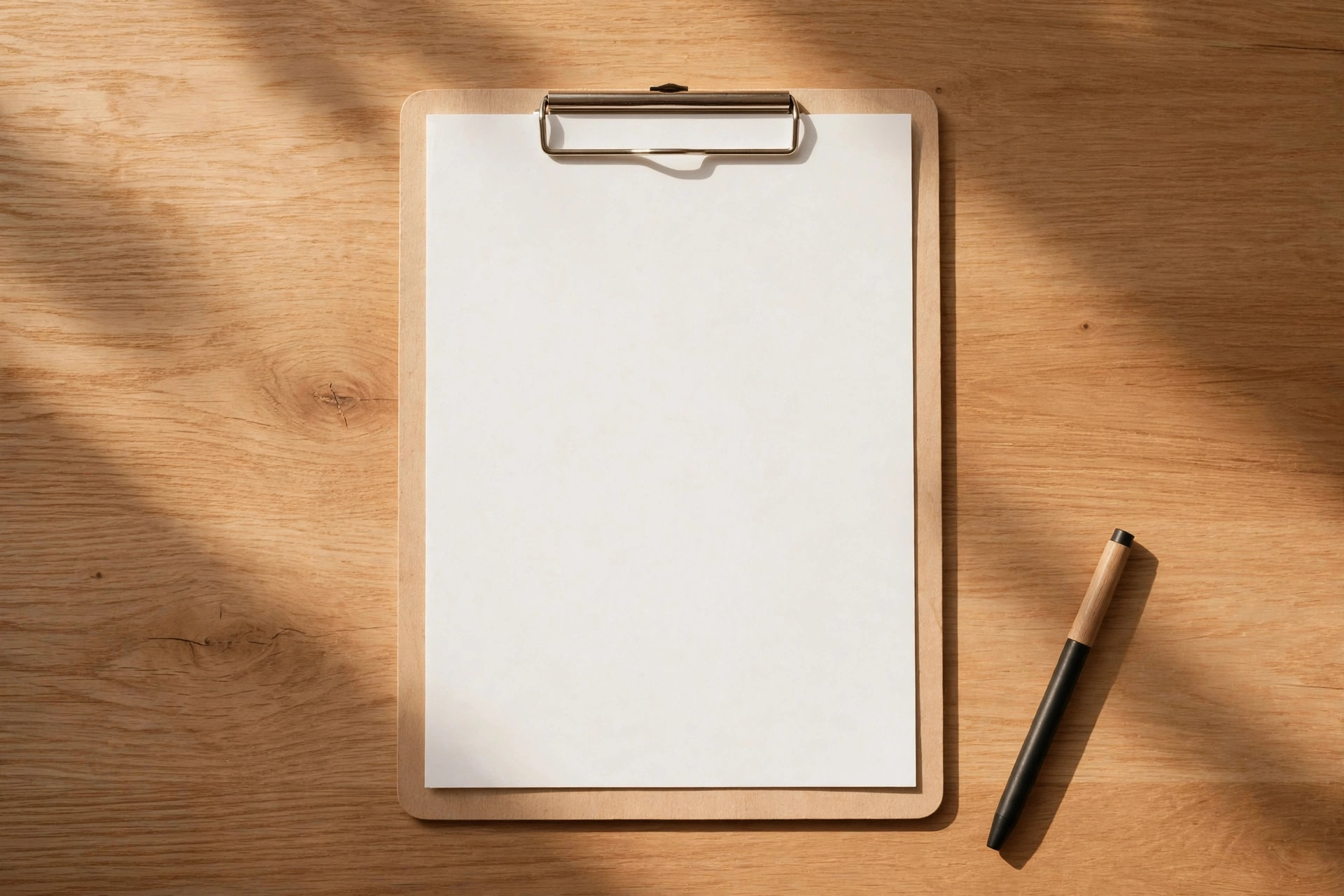 Clipboard with blank paper and a pen on a wooden desk