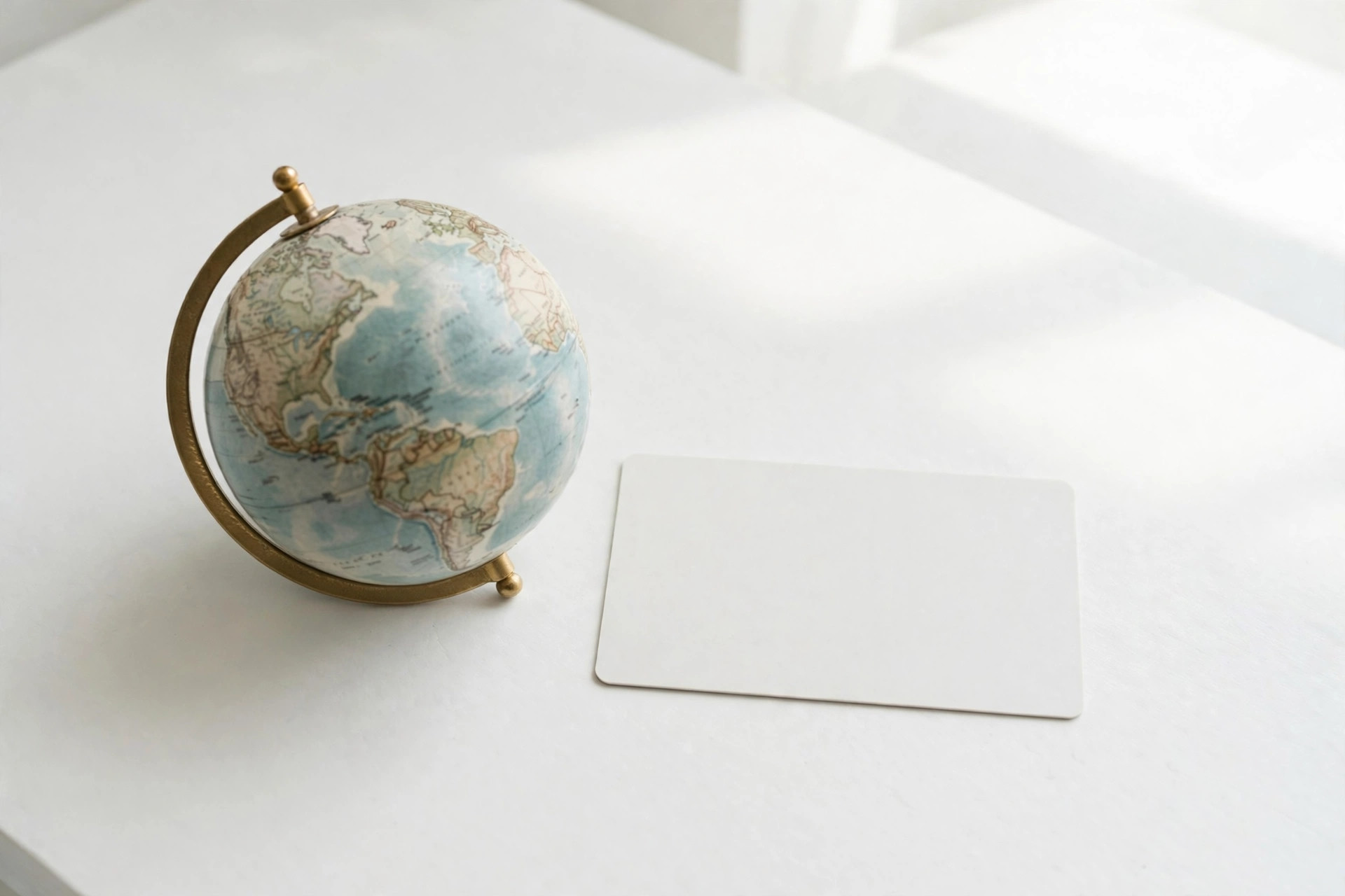 Small desktop globe beside a blank card on a white desk