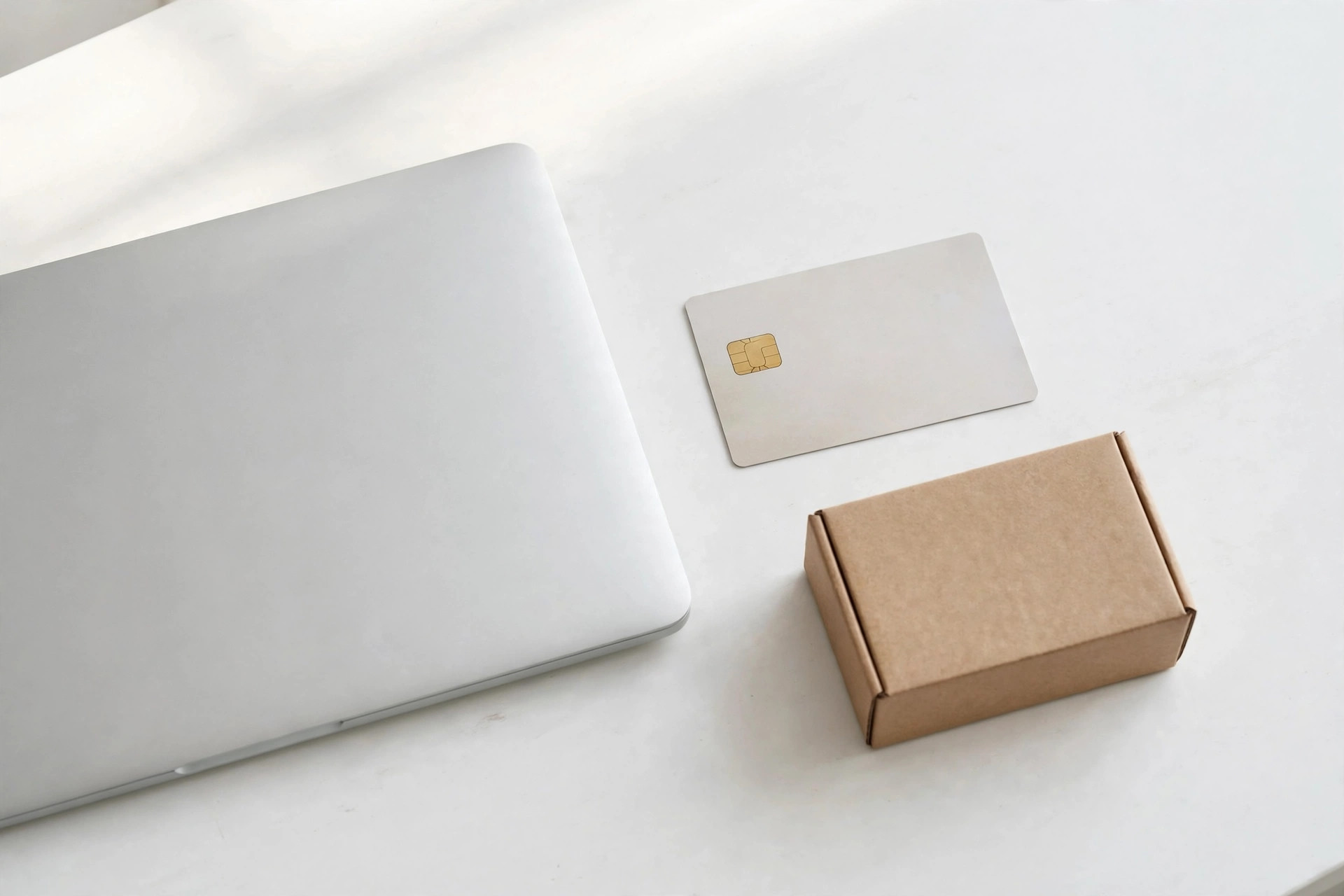 A closed laptop, a chip credit card, and a small cardboard shipping box on a desk