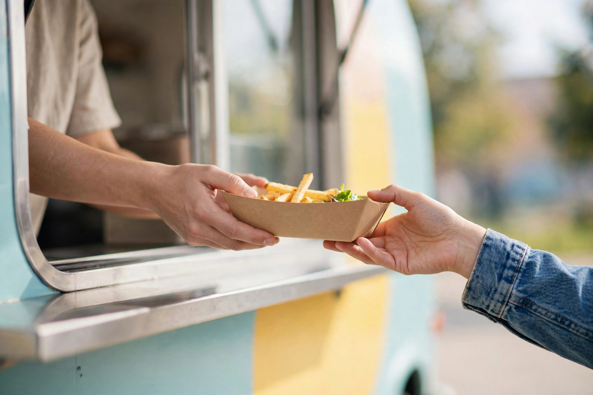 Food truck worker handing a paper tray of fries through the serving window