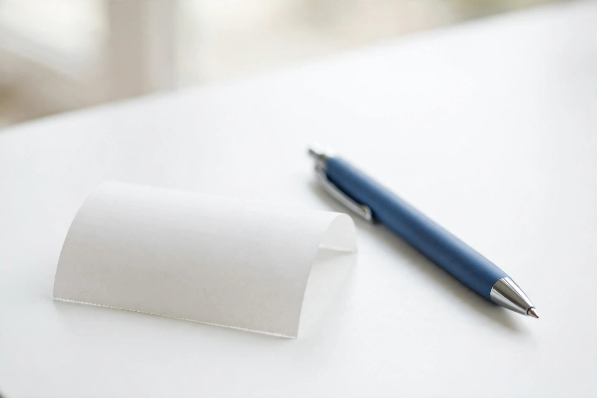 Blank curled paper receipt and a blue pen on a white desk