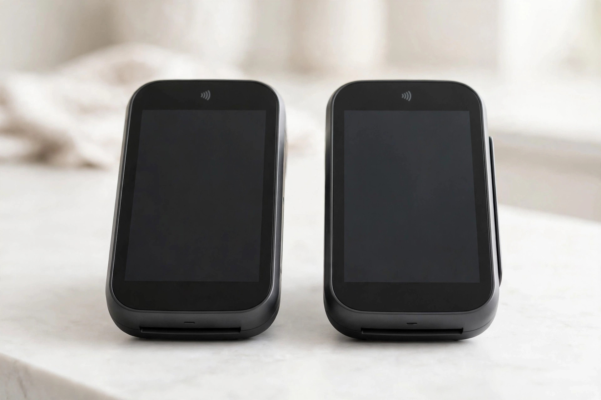 Two card payment terminals with blank screens side by side on a counter