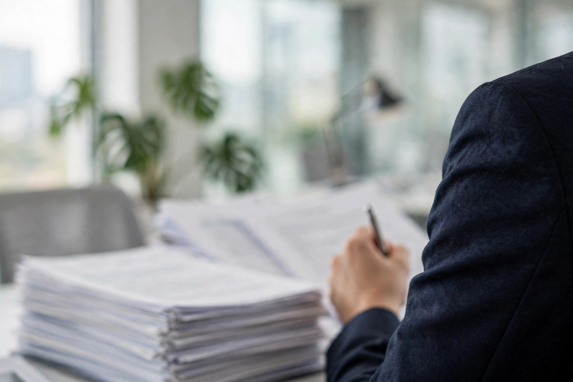 A business person reviewing a thick stack of paperwork with a pen, documents out of focus.